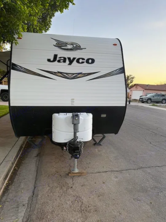 Jayco RV rental travel trailer parked on a residential street. Front view showing the hitch, propane tanks, and stabilizer jacks.. Jayco Jay Flight SLX Baja Edition 2019