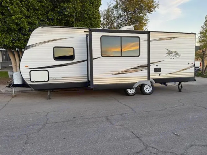 This white travel trailer RV rental, with its slide-out extended, is ready for adventure. It's parked on an asphalt surface.. Jayco Jay Flight SLX Baja Edition 2019