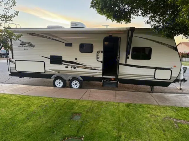 Light-colored Jay Flight SLX RV rental travel trailer parked street-side with an extended awning under a sunset sky.. Jayco Jay Flight SLX Baja Edition 2019
