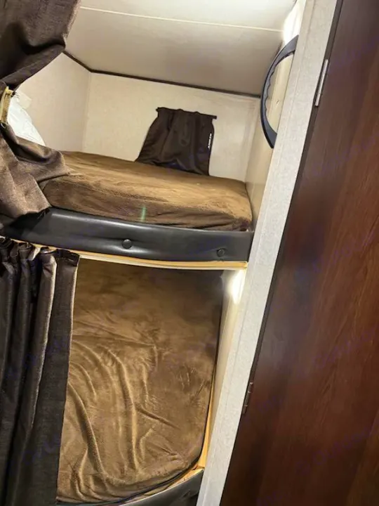 Compact bunk beds in an rv rental, featuring brown blankets and curtains, provide cozy sleeping space.. Jayco Jay Flight SLX Baja Edition 2019