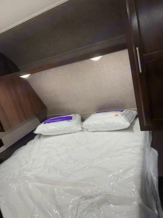 Cozy RV rental bedroom with a new, plastic-covered mattress and pillows, featuring built-in overhead lighting and storage.. Jayco Jay Flight SLX Baja Edition 2019