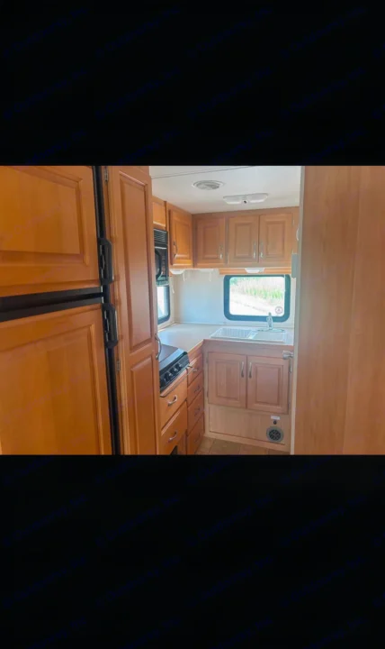 RV rental kitchen with warm wood cabinets, stove, sink, fridge, and microwave, offering a cozy and functional space.. Triple E Regency 2006