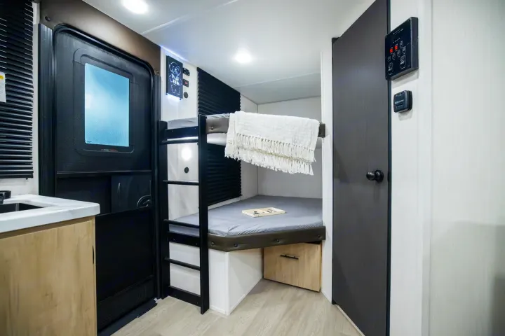 Inside a compact RV rental, showcasing cozy bunk beds, an entrance door, and utility controls for comfortable travel.. Forest River Campsite Reserve 17LS 2026