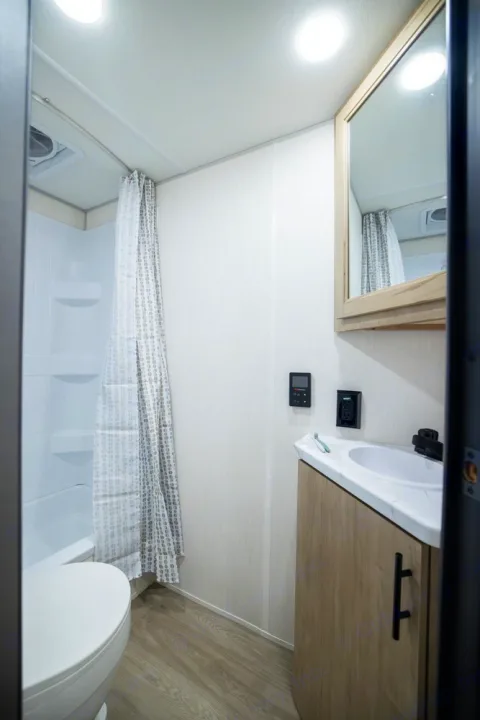 RV rental's clean bathroom features a shower, toilet, sink vanity with mirror, and wood-look flooring.. Forest River Campsite Reserve 17LS 2026