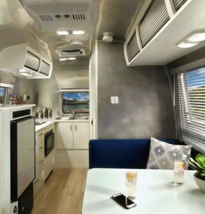 Modern RV rental interior showing a compact kitchen, dining nook, and scenic window views. Sleek design, ideal for travel.. Airstream Bambi 2024