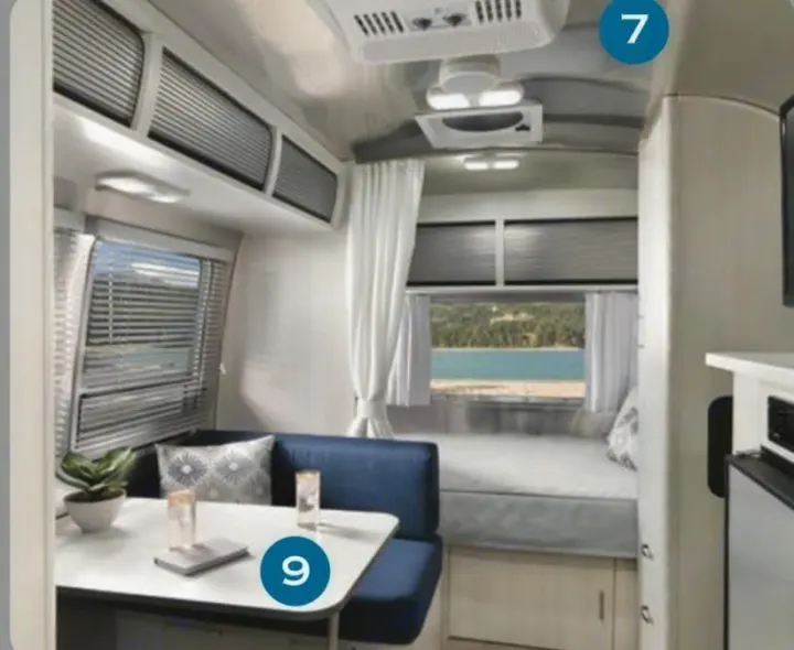 Modern rv rental interior: bright dinette with blue cushions, overhead storage, and a cozy bed overlooking a lake.. Airstream Bambi 2024