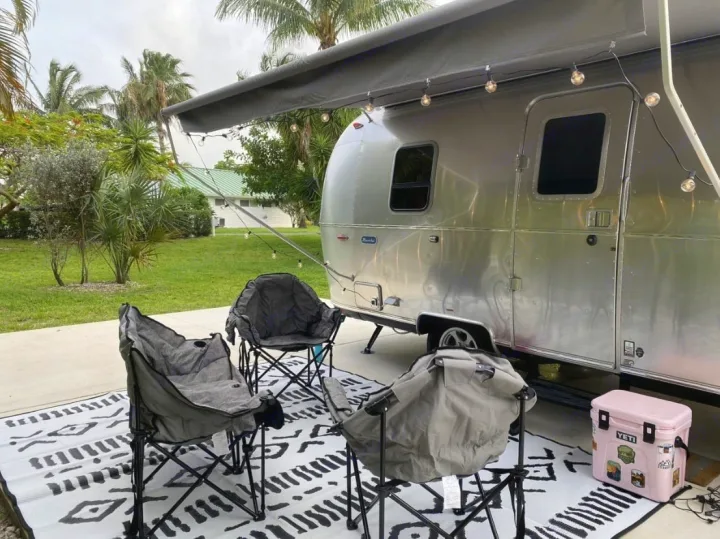 Perfect rv rental getaway setup: Airstream, string lights under awning, comfy camping chairs on an outdoor rug, and a pink cooler.. Airstream Bambi 2024