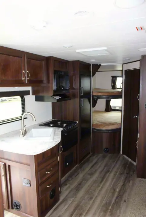 Interior of an RV rental showing a compact kitchen with sink, stove, microwave, and bunk beds in the back.. Jayco Jay Flight SLX 2018