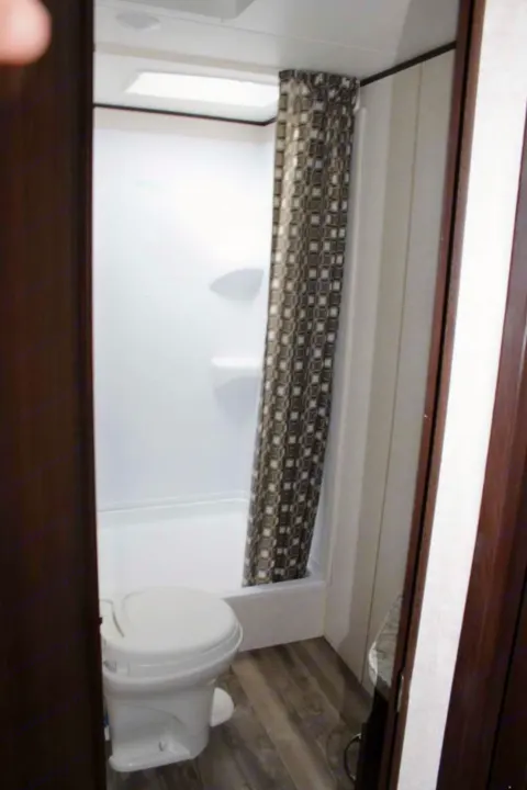 RV rental bathroom: functional shower and toilet setup, featuring a patterned curtain and compact design.. Jayco Jay Flight SLX 2018