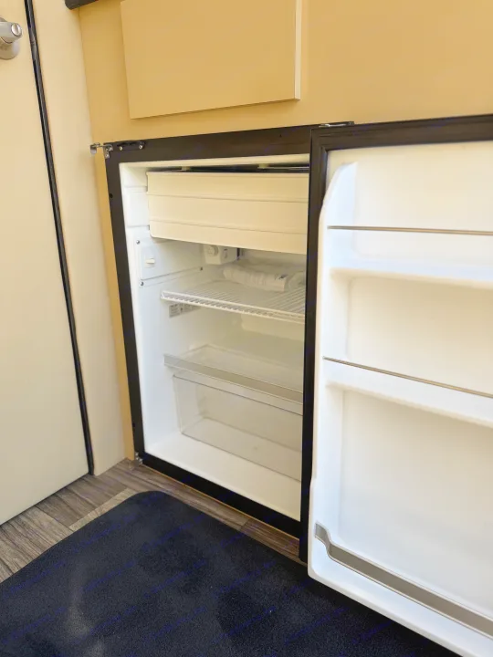 Clean, open mini-fridge in an rv rental, showing freezer, wire shelf, pull-out bin, and door storage.. Ultimate Toys Ultimate Coach 2024