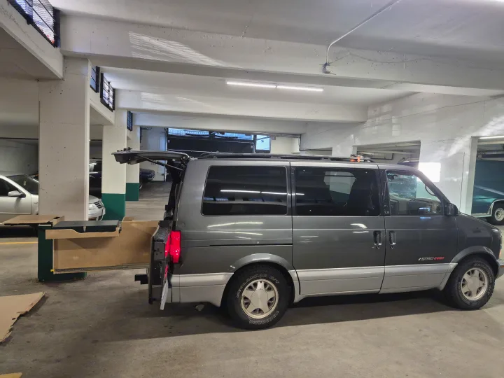Customized Astro AWD camper van, rear hatch open revealing storage. Parked in garage, ideal for adventures or rv rental.. Chevrolet Astro 1999