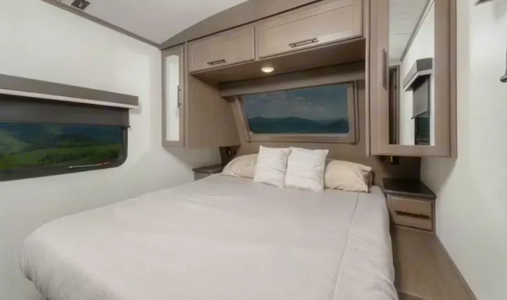 Cozy RV rental bedroom with queen bed, scenic windows, and ample storage. Ideal for comfortable travel adventures.. Keystone RV Cougar 2022