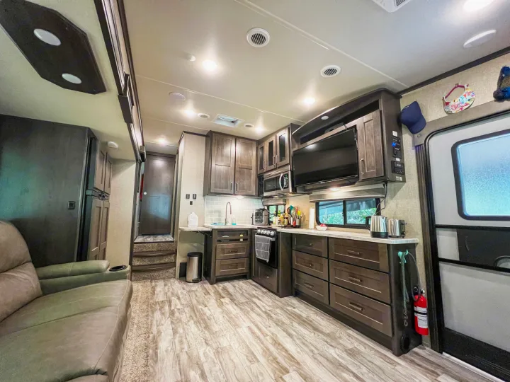 An RV rental's spacious interior showcasing a well-equipped kitchen with dark wood cabinets, a comfy sofa, and light flooring.. Keystone RV Cougar 2022