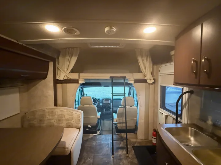 Cozy RV rental interior showcasing dinette, kitchenette, bunk, and cockpit area, complete with a fire extinguisher.. Winnebago View 2014
