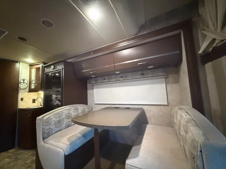 This cozy RV rental interior features a dinette with booth seating, overhead cabinets, and a compact kitchen area with a sink.. Winnebago View 2014