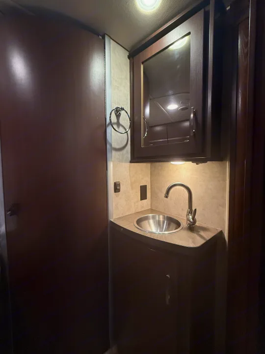 RV rental bathroom: dark vanity, stainless steel sink, chrome faucet, mirrored cabinet, and towel ring. Under-cabinet lighting.. Winnebago View 2014
