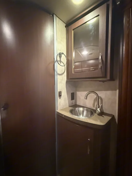 Compact rv rental bathroom with a stainless steel sink, modern faucet, mirrored cabinet, and storage. Functional for travel.. Winnebago View 2014