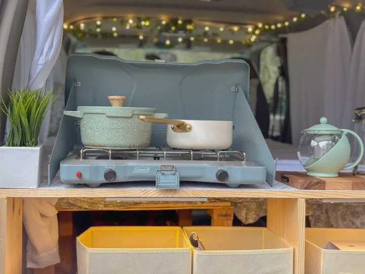 Cozy RV rental cooking area with a Coleman stove, pots, teapot, and plant. Perfect for van life meals.. Chevrolet astro 2000