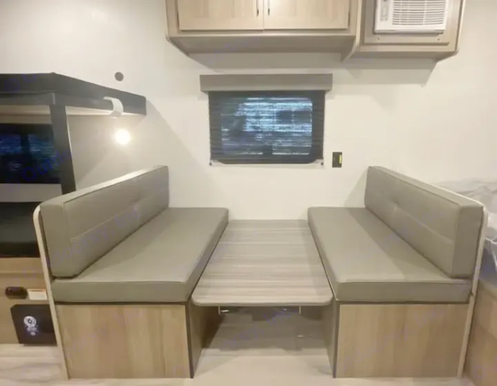 Modern RV rental interior: A bright dinette with grey cushioned benches, a light wood table, and an adjacent bunk bed.. Keystone RV Coleman 2025