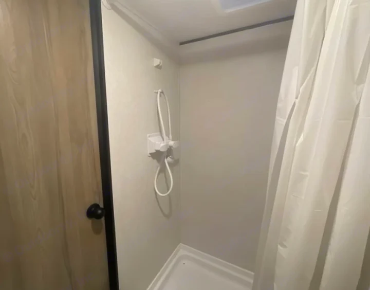 Clean, compact shower in an RV rental, featuring a handheld sprayer and white curtain.. Keystone RV Flagstaff Super Lite 2023