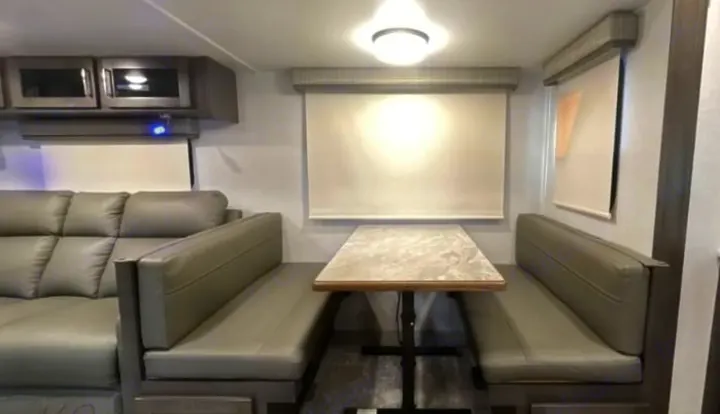 RV rental interior: gray sectional sofa, dinette with bench seating & table, overhead cabinets, and window blinds.. Keystone RV Flagstaff Super Lite 2023