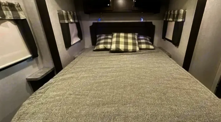 Cozy RV rental bedroom: large bed with plaid pillows, storage cabinets, and side windows. Perfect for road trips.. Keystone RV Flagstaff Super Lite 2023
