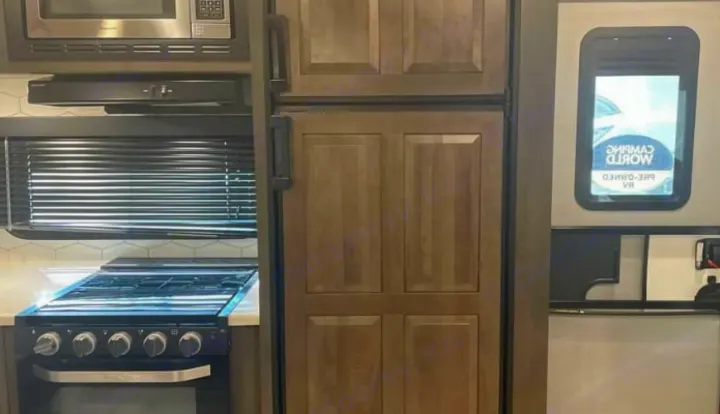 Compact RV rental kitchen with microwave, stove, and wood-paneled refrigerator for on-the-go cooking.. Keystone RV Flagstaff Super Lite 2023