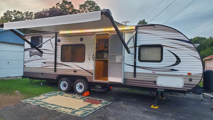 Experience outdoor living! This RV rental features an illuminated awning and open door, perfect for your next camping trip.. Forest River Wildwood X-Lite 2018