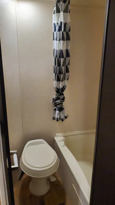 Compact RV rental bathroom featuring a toilet, small bathtub, and a black/white/gray geometric shower curtain.. Forest River Wildwood X-Lite 2018