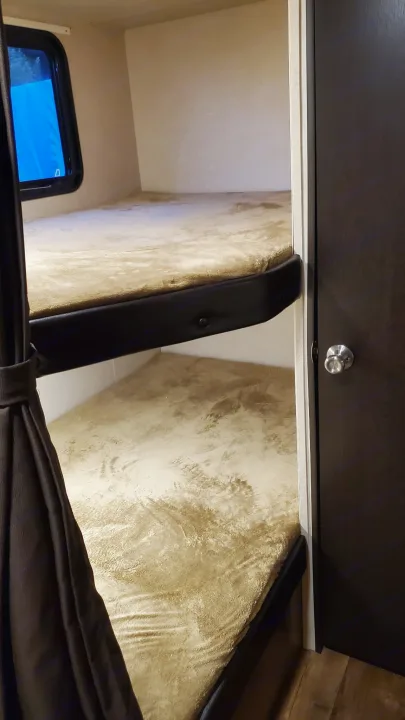 Compact sleeping area in an RV rental, featuring two bunk beds with soft covers, a window, and a door.. Forest River Wildwood X-Lite 2018