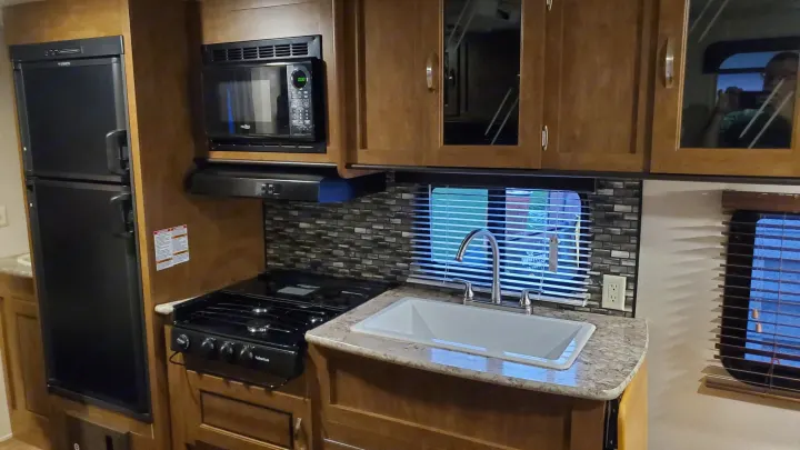 This clean RV rental kitchen offers a fridge, microwave, gas stove, sink, and wooden cabinets for your travels.. Forest River Wildwood X-Lite 2018