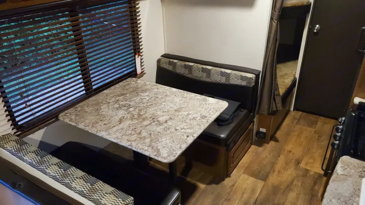 Cozy RV rental interior: dinette with patterned table, dark benches, window blinds, next to bunk and kitchen.. Forest River Wildwood X-Lite 2018