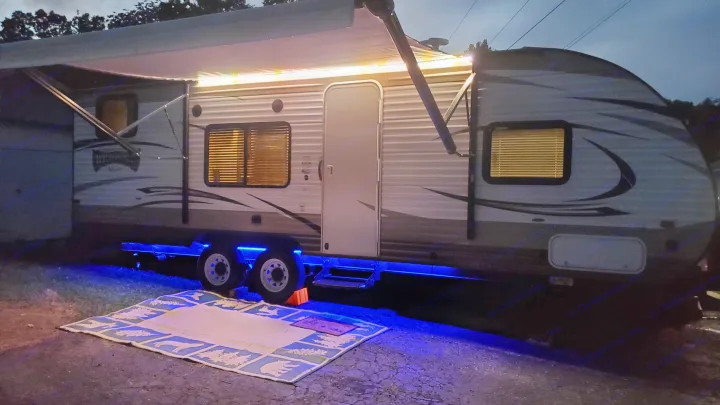 Night camping setup with an RV rental: Awning extended, colorful LED lights above, and vibrant blue undercarriage glow.. Forest River Wildwood X-Lite 2018