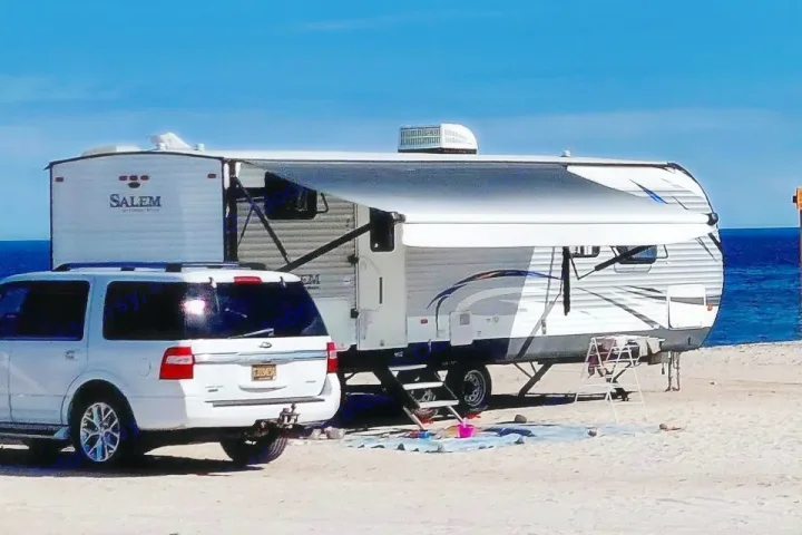 RV rental parked on a sandy beach next to a white SUV, with the ocean in the background, awning extended for shade. Perfect beach camping.. Forest River Salem 2018