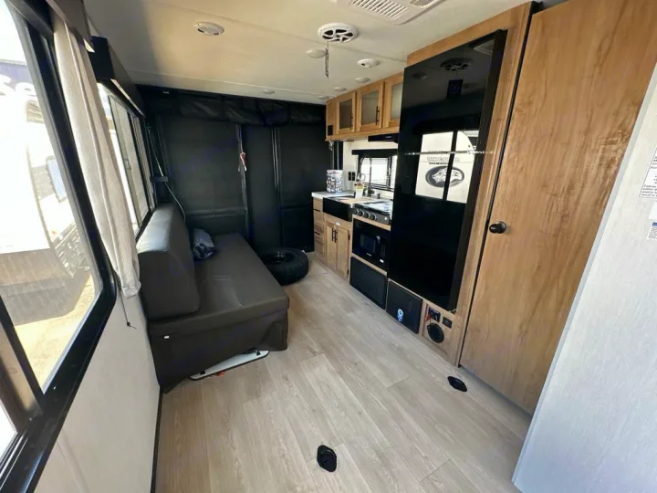 Step inside this RV rental's modern interior. Light wood-look floor, large windows, a dark sofa, and a compact kitchen with a black fridge.. Forest River Cherokee Grey Wolf 2025