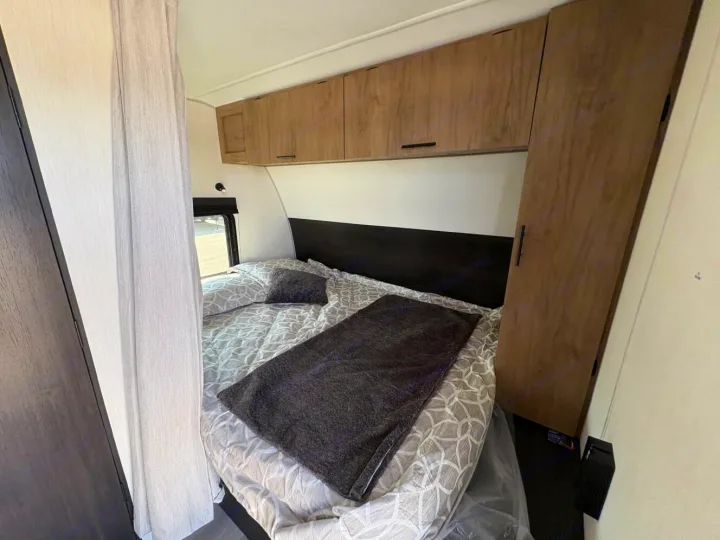 Cozy RV rental bedroom features a patterned bed, dark throw, overhead cabinets, and wardrobe. Perfect for your travels!. Forest River Cherokee Grey Wolf 2025