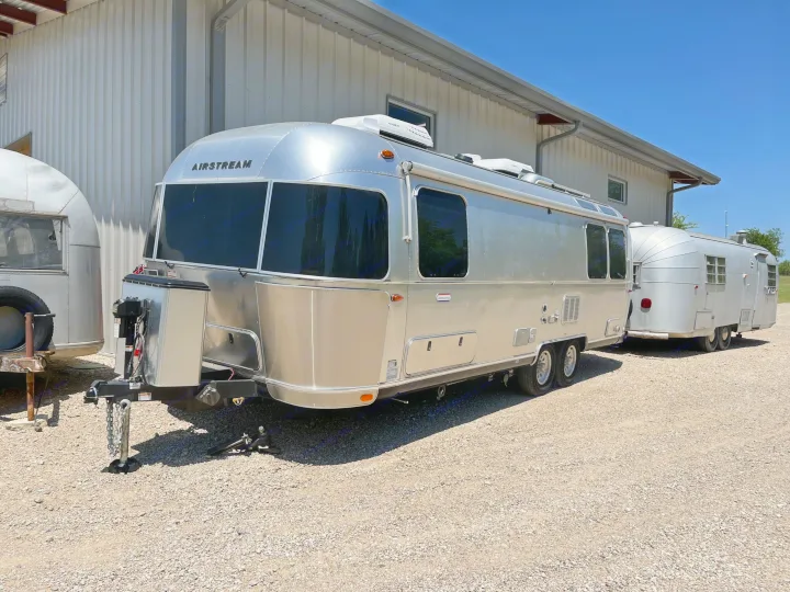 Shiny modern and vintage Airstream travel trailers for an rv rental, parked on gravel next to a metal building.. Airstream International 2021