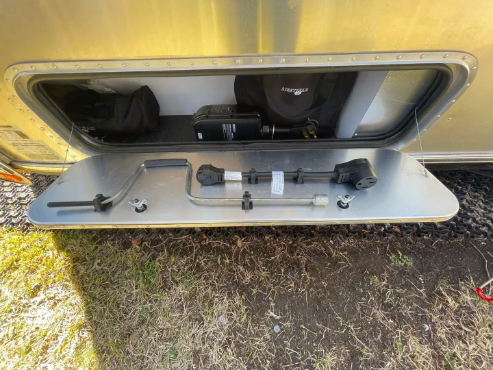 Airstream RV rental exterior storage open, showing a power adapter, stabilizer crank, and branded bag.. Airstream International 2021