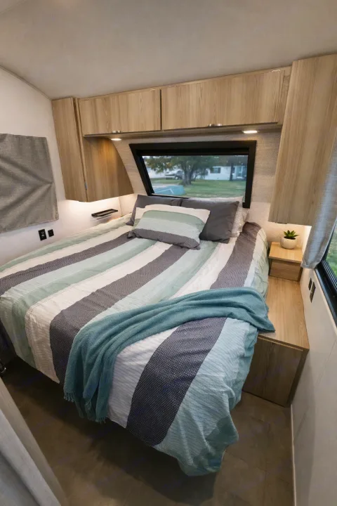 Modern RV rental bedroom with striped bedding, ample storage, and a scenic window view. Ideal for road trip comfort.. Forest River Wildwood FSX Platinum 2023