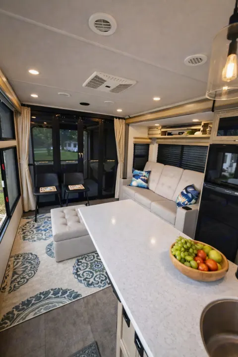 Spacious RV rental interior: modern living area & kitchen featuring a comfy sofa, large counter with fruit, and bright windows.. Forest River Wildwood FSX Platinum 2023