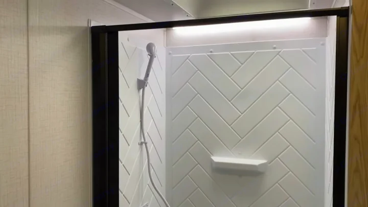 Interior of an RV rental shower featuring stylish white herringbone walls, a handheld showerhead, and an overhead LED light.. Forest River Wildwood FSX Platinum 2023