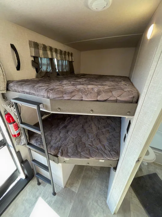 Cozy bunk beds in an RV rental, featuring a ladder, soft grey bedding, and a fire extinguisher for safety.. Forest River Flagstaff Super Lite 2021