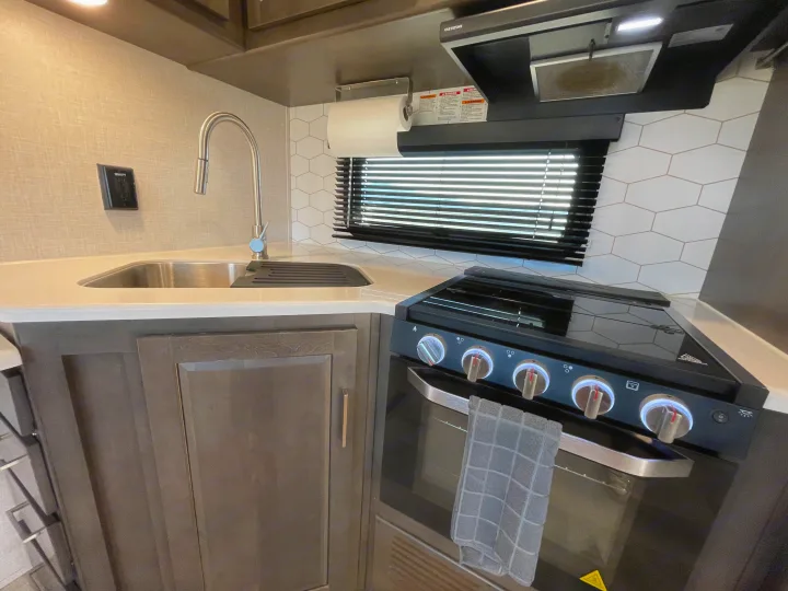 Compact RV rental kitchen with stainless steel sink, black stove/oven, hex tile backsplash, and window. Towel on oven handle.. Forest River Flagstaff Super Lite 2021