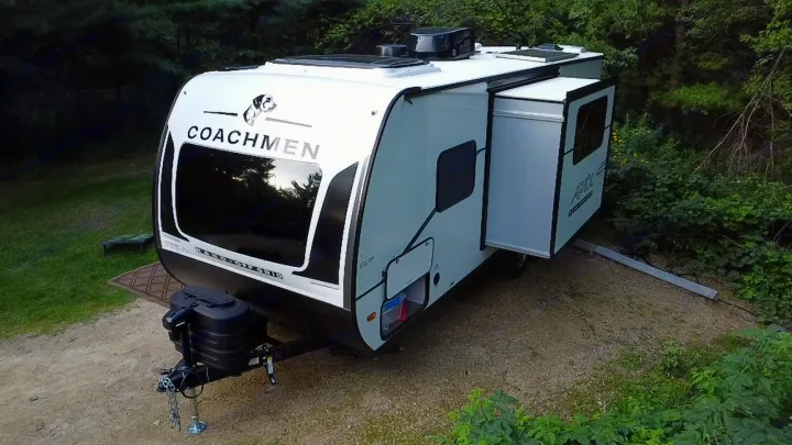 This RV rental, a Coachmen travel trailer, is set up at a wooded campsite, ready for an outdoor adventure.. Coachmen Apex Nano 2025