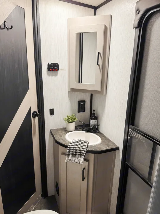 Compact RV rental bathroom features a corner sink, mirror cabinet, modern black fixtures, and subtle decor.. Heartland Mallard M312 2022
