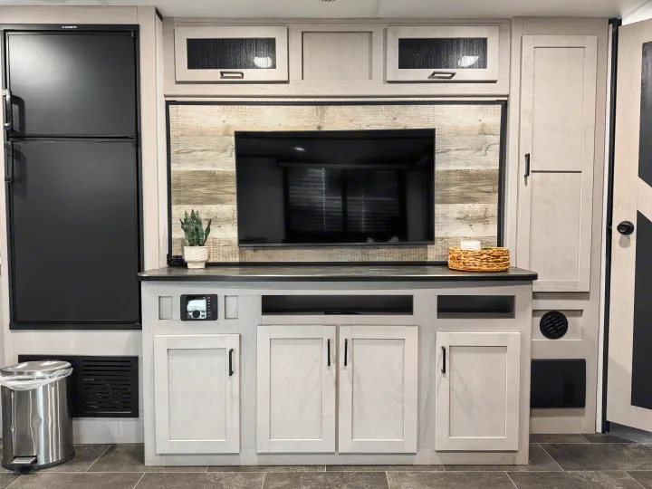 RV rental's modern living area featuring an entertainment center with a TV, a Dometic fridge, and light wood cabinets.. Heartland Mallard M312 2022