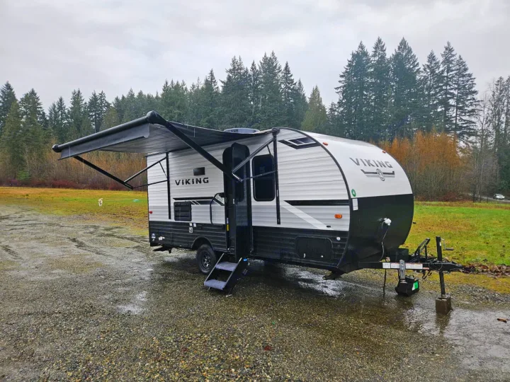 Experience adventure! This Viking travel trailer RV rental, with awning extended, is ready for camping on a damp, overcast day.. Forest River Viking 4K 2023
