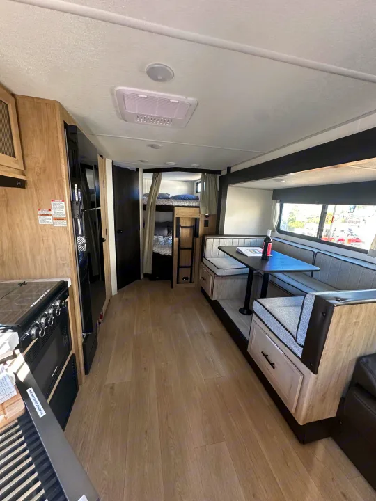 Modern RV rental interior: kitchen with stove, dinette, and bunk beds in light wood and black trim. Light flooring and ceiling AC.. Forest River Cherokee Grey Wolf 2026