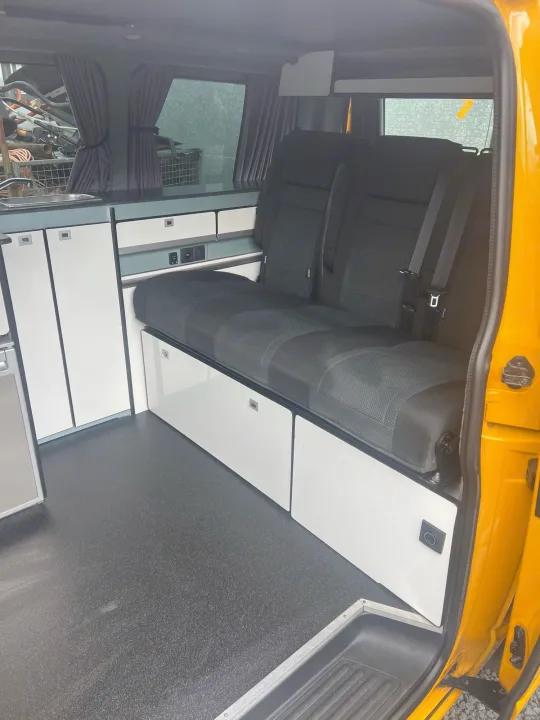 Inside this yellow rv rental campervan: a versatile bench seat, ample storage cabinets, and a sink, all on a dark floor.. Volkswagen T6 transporter 2019