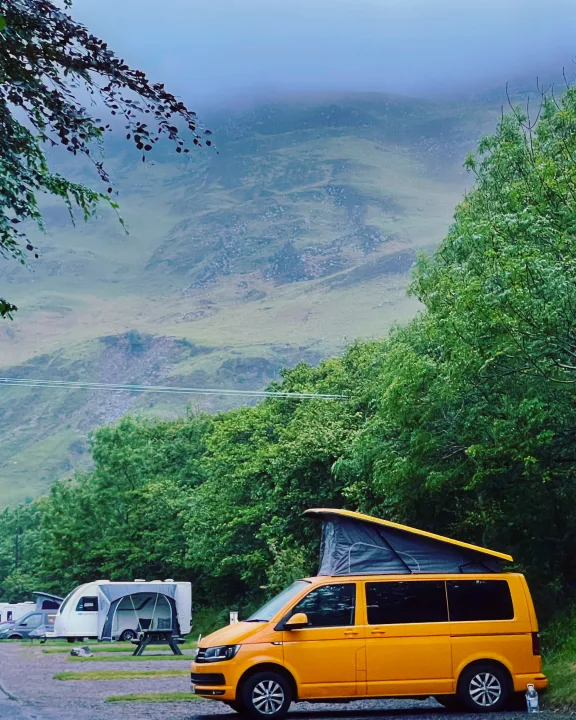 Yellow campervan with pop-top at a scenic rv rental campsite surrounded by misty mountains and lush trees.. Volkswagen T6 transporter 2019